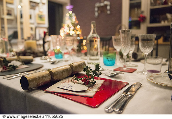 Ein gedeckter Tisch für ein Weihnachtsessen  mit Silber- und Kristallgläsern und einem Weihnachtsbaum im Hintergrund.