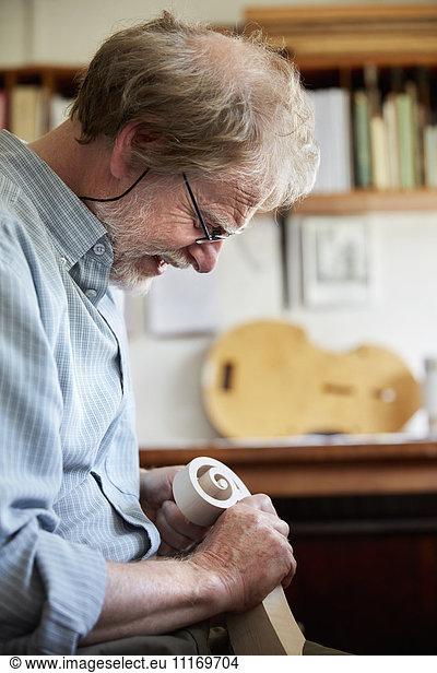 Ein Geigenbauer  der mit Handwerkzeugen eine neue hölzerne Geigenkopfplatte glättet und fertigstellt  gewellte Schnecke aus Holz.