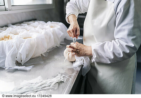 Ein gelernter Koch wickelt in der Fabrik Käse in ein Tuch ein