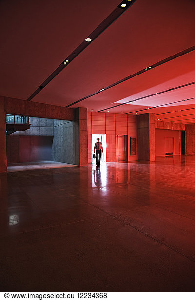 Ein Geschäftsmann geht durch die Tür eines Lobbybereichs  der durch rot getöntes Glas vom Tageslicht erhellt wird.