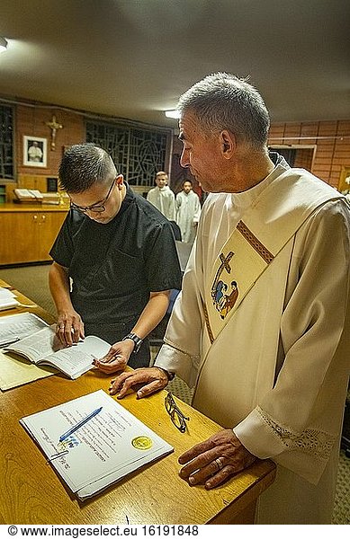 Ein in ein weißes Gewand gekleideter Diakon unterhält sich mit dem hispanischen Priester einer katholischen Kirche in Südkalifornien  um sich auf die Assistenz bei einer Messe vorzubereiten.