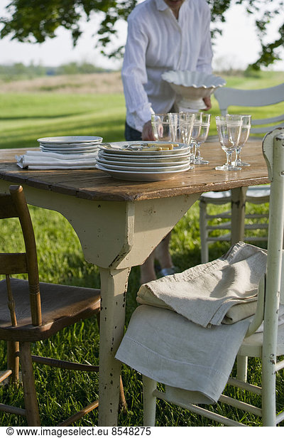 Ein in einem Garten gedeckter Tisch mit weißem Porzellangeschirr und Besteck. Sommer.