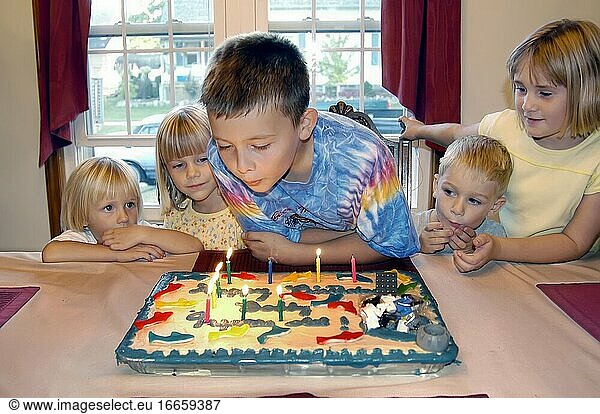 Ein 9-jähriger Junge feiert seinen Geburtstag mit einer Party mit Freunden  bei der Geschenke und ein Kuchen mit Kerzen verteilt werden.