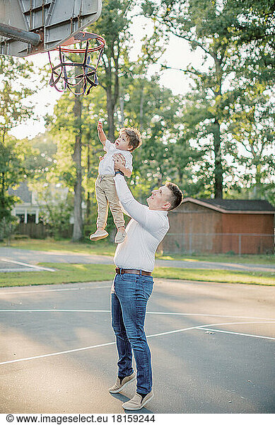 Ein 30-35 Jahre alter Vater hebt seinen 2-jährigen Sohn zum Basketballnetz.