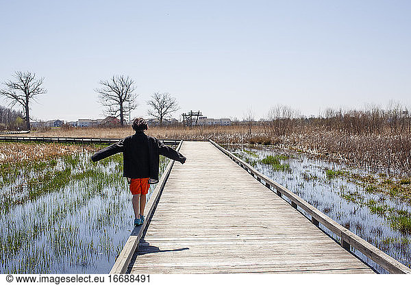 Ein Junge geht am Rande einer Holzbrücke über ein Feuchtgebiet im Frühling