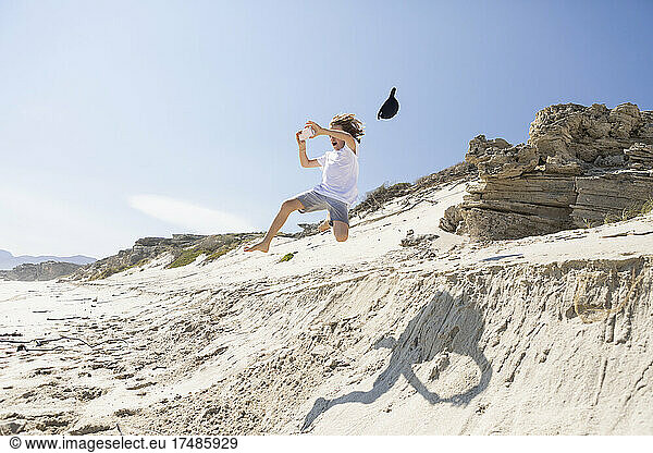 Ein Junge springt von einer Sanddüne in den weichen Sand darunter.