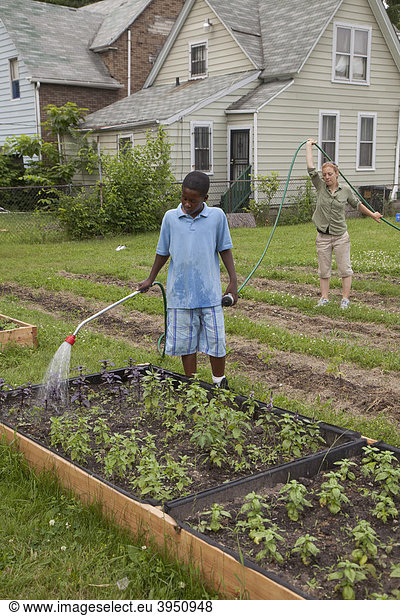 Ein Junge wässert Pflanzen  unterstützt von einer Aufsichtsperson  in einem Programm namens Growing Healthy Kids für Kinder im Alter von 5-11 Jahren  in einem Earthworks Urban Garden Garten  in dem Nahrung für die Capuchin Soup Kitchen Suppenküche angebaut wird  Detroit  Michigan  USA