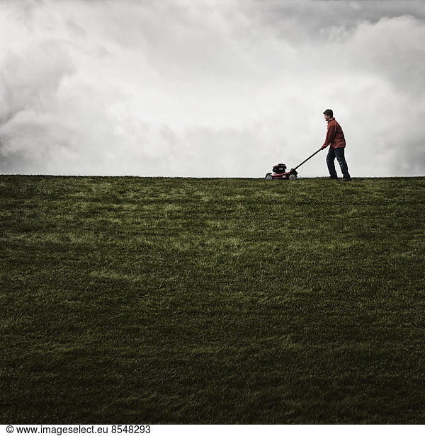 Ein junger Mann mäht das Gras auf einem Grundstück und pflegt den Garten mit einem Benzinrasenmäher.