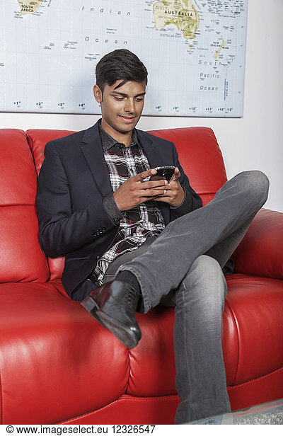 Ein junger Millennial-Geschäftsmann benutzt sein Smartphone in der Lobby eines Arbeitsplatzes; Sherwood Park  Alberta  Kanada