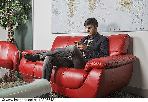 Ein junger Millennial-Geschäftsmann benutzt sein Smartphone in der Lobby eines Arbeitsplatzes; Sherwood Park  Alberta  Kanada