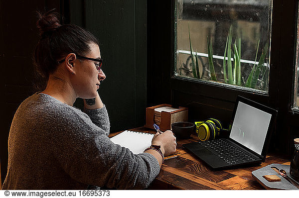 Ein junger Student arbeitet an einem Tisch in der Nähe eines Kneipenfensters. Nahaufnahme