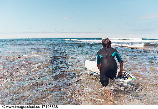 Ein junger Surfer steigt ins Wasser und beobachtet andere Surfer.