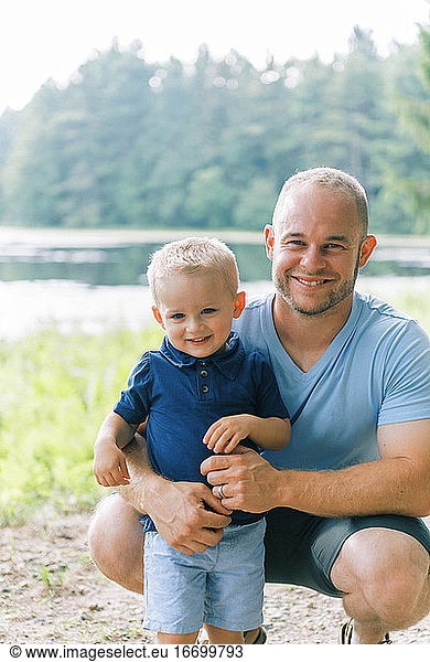 Ein junger Vater umarmt seinen zwei Jahre alten Sohn  während beide lächeln