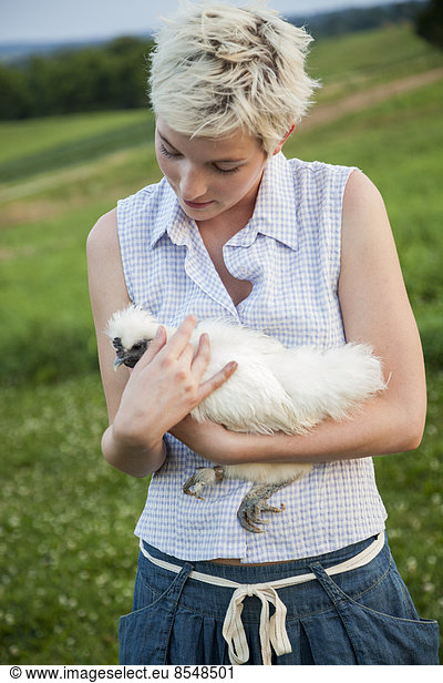 Ein junges Mädchen  ein Teenager  hält ein Huhn mit weißen Federn in den Armen.