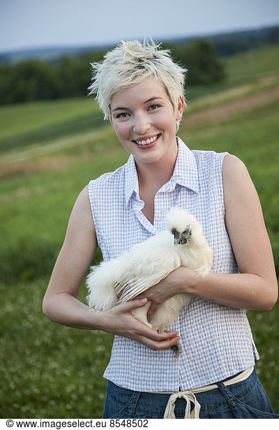 Ein junges Mädchen  ein Teenager  hält ein Huhn mit weißen Federn in den Armen.