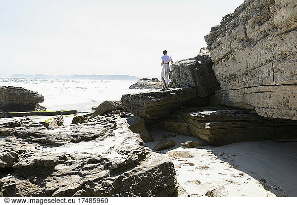 Ein junges Mädchen erkundet die Klippen und Felsen an einem Strand an der Atlantikküste.