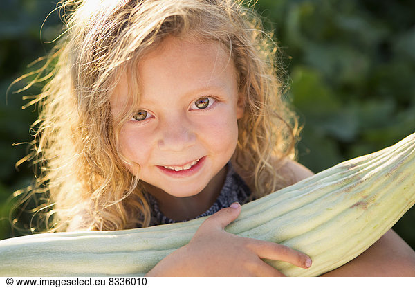 Ein junges Mädchen mit langen roten Locken im Freien in einem Garten  das einen großen frischen Maiskolben mit Maiskolben in der Hand hält.