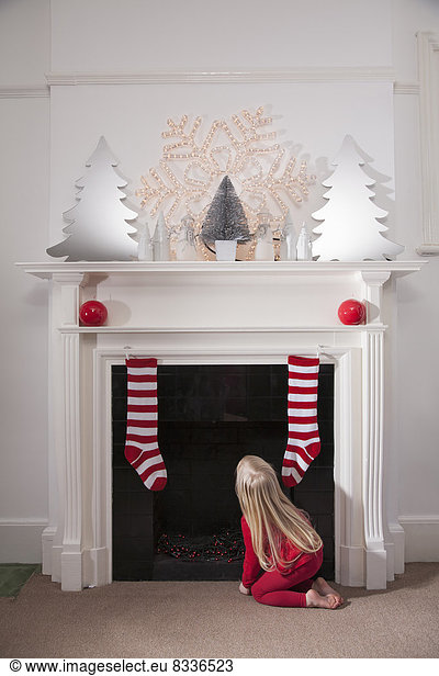 Ein junges Mädchen schaut erwartungsvoll den Schornstein hinauf und wartet auf die Ankunft des Weihnachtsmanns.