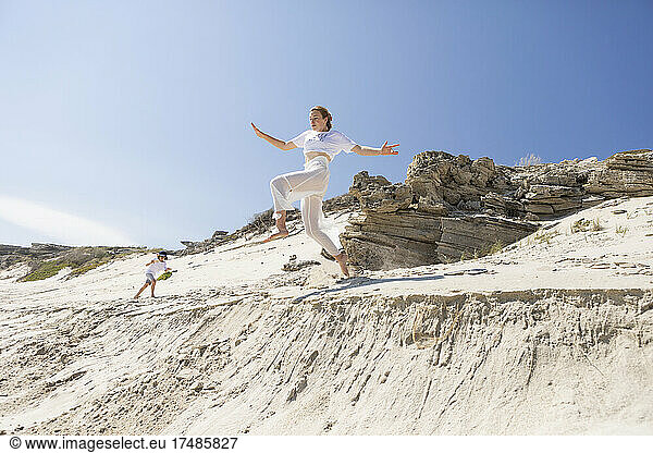 Ein junges Mädchen springt von einer Sanddüne in den weichen Sand darunter.