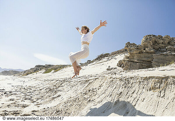 Ein junges Mädchen springt von einer Sanddüne in den weichen Sand darunter.