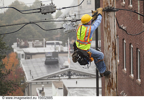 Ein Kabelmonteur hält sich am Mast fest  während er die Spannung mit Hilfe von Spikes einstellt