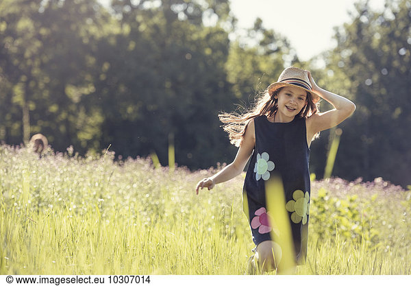 Ein Kind  ein junges Mädchen mit Strohhut auf einer Wiese mit Wildblumen im Sommer.