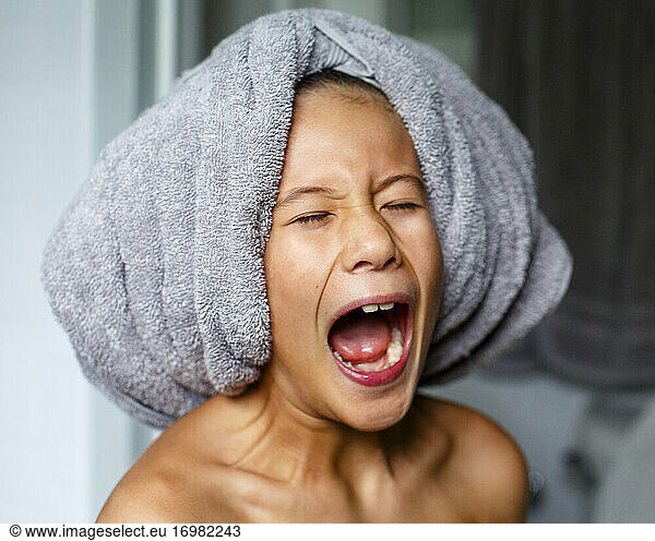 Ein Kind mit Badetuch auf dem Kopf schreit spielerisch mit weit geöffnetem Mund