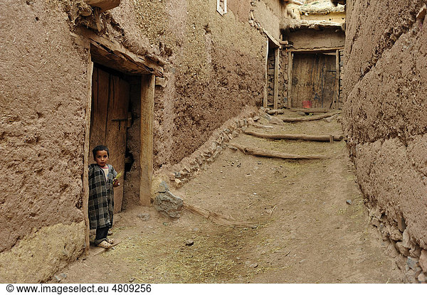 Ein kleiner Berberjunge steht vor der Haustür in einer schmalen Gasse in einem Lehmdorf  Kelaa M`gouna  Hoher Atlas  Marokko  Afrika
