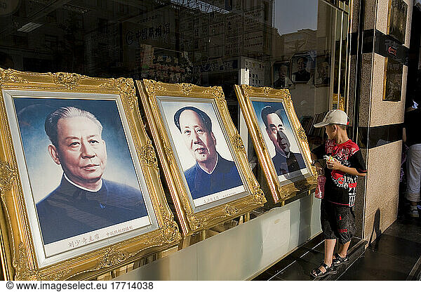 Ein kleiner Junge betrachtet die Porträts von Chinas Staatsoberhäuptern  während seine Mutter in einem angrenzenden Geschäft einkauft  Peking  China