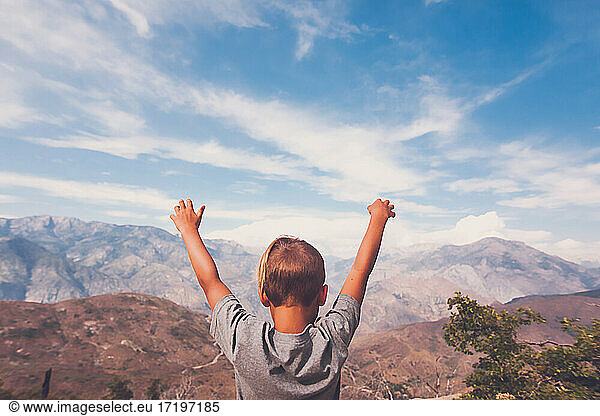Ein kleiner Junge genießt die Aussicht auf die Berge mit weit ausgebreiteten Armen.