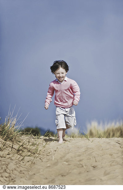 Ein kleiner Junge mit braunen Haaren  der am Strand läuft.