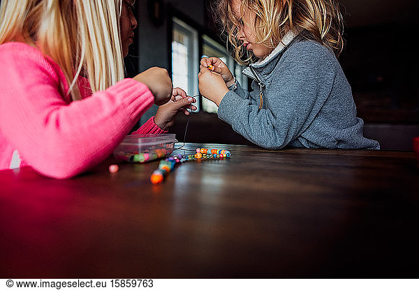 Ein kleiner Junge und ein kleines Mädchen  die an einem Tisch eine Perlenkette herstellen