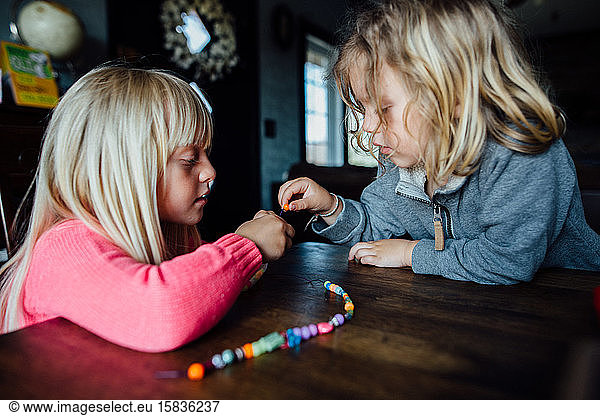 Ein kleiner Junge und ein kleines Mädchen  die tagsüber bei Tisch Perlenketten herstellen