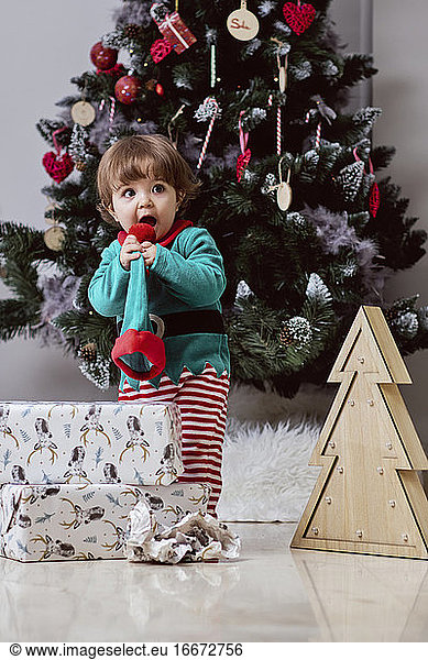 Ein kleiner 12 Monate alter Weihnachtself mit einem Weihnachtsbaum und Geschenken