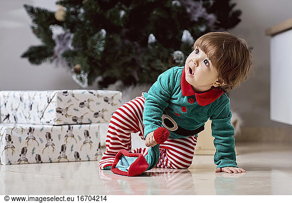 Ein kleiner 12 Monate alter Weihnachtself mit einem Weihnachtsbaum und Geschenken
