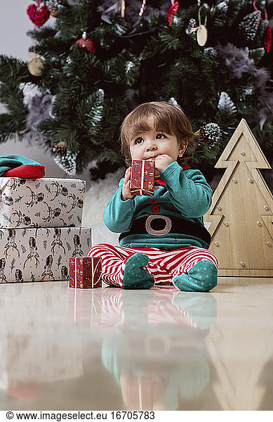 Ein kleiner 12 Monate alter Weihnachtself mit einem Weihnachtsbaum und Geschenken