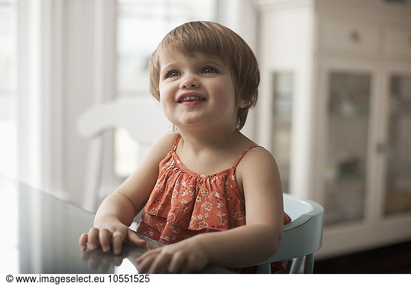 Ein kleines Kind  ein Mädchen  das an einem Tisch sitzt  aufschaut und lächelt.
