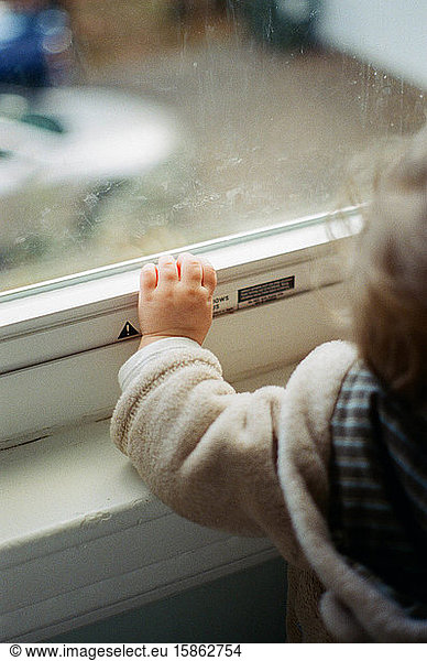 Ein kleines Mädchen  das ein Fenster berührt.
