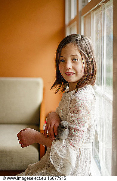 Ein kleines Mädchen mit fehlenden Zähnen sitzt mit einem Küken auf dem Arm