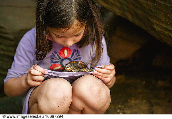 Ein kleines Mädchen mit schmutzigen Knien hält eine kleine Schildkröte auf dem Schoß