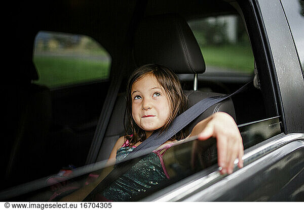 Ein kleines Mädchen sitzt lächelnd in einem Auto und streckt den Arm aus dem Fenster