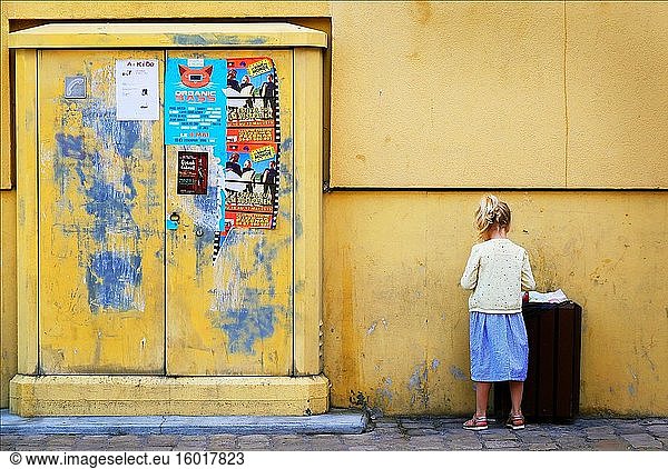Ein kleines Mädchen steht an einer gelben Wand.