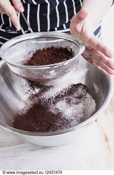 Ein Koch  der Kakaopulver in eine Metallschüssel mit Mehl und Kuchenzutaten sieben lässt.