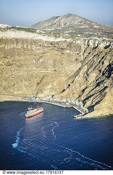 Ein Kreuzfahrtschiff nähert sich dem Hafen von Oia an der Küste am Fuße einer steilen Klippe auf der griechischen Insel.