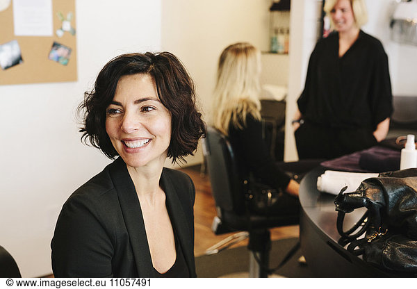 Ein Kunde sitzt in einem Friseursalon  mit zwei Personen im Hintergrund.