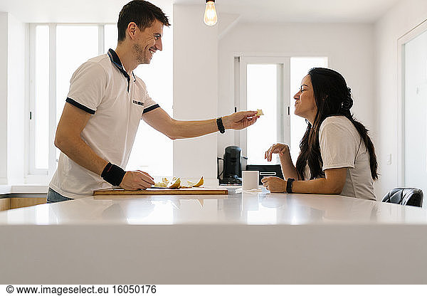 Ein lächelnder Mann füttert eine Frau in der Küche mit Obst
