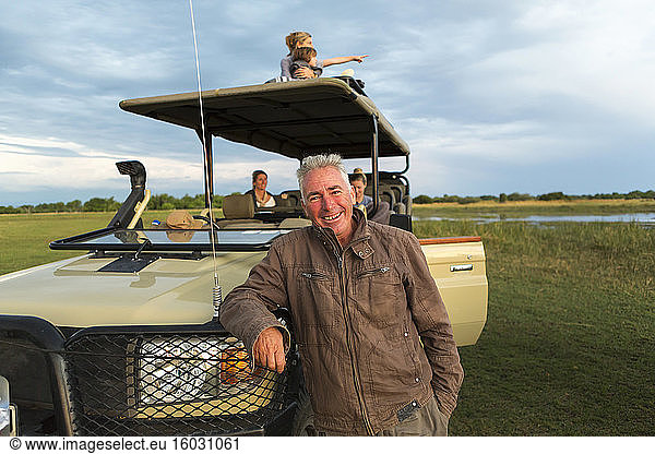 Ein lächelnder Safari-Führer und eine Familie von Touristen in einem Safari-Fahrzeug.