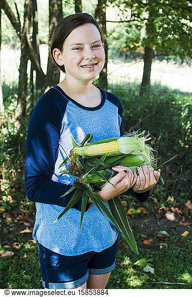 Ein lächelndes Mädchen trägt Zuckermais aus einem Garten in Michigan