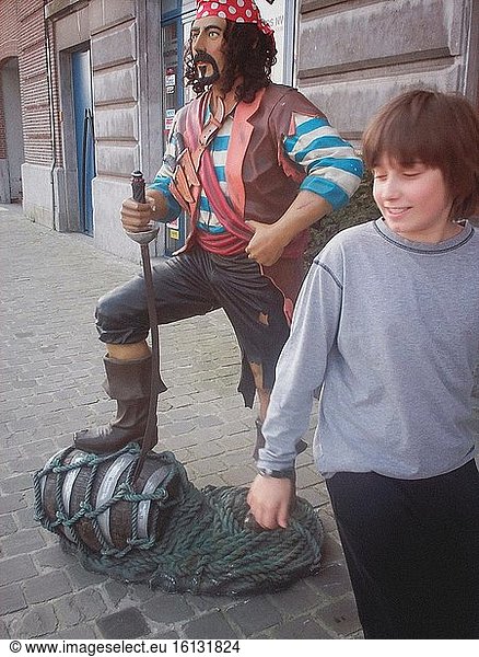 Ein leger gekleideter Junge lacht  als er ein farbenfrohes Modell eines Seeräubers in Antwerpen  Belgien  betrachtet.