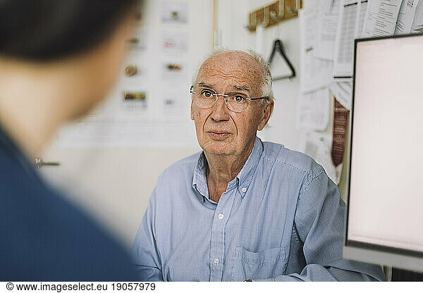 Ein älterer männlicher Patient trägt eine Brille und hört einer Krankenschwester beim Besuch in der Klinik zu